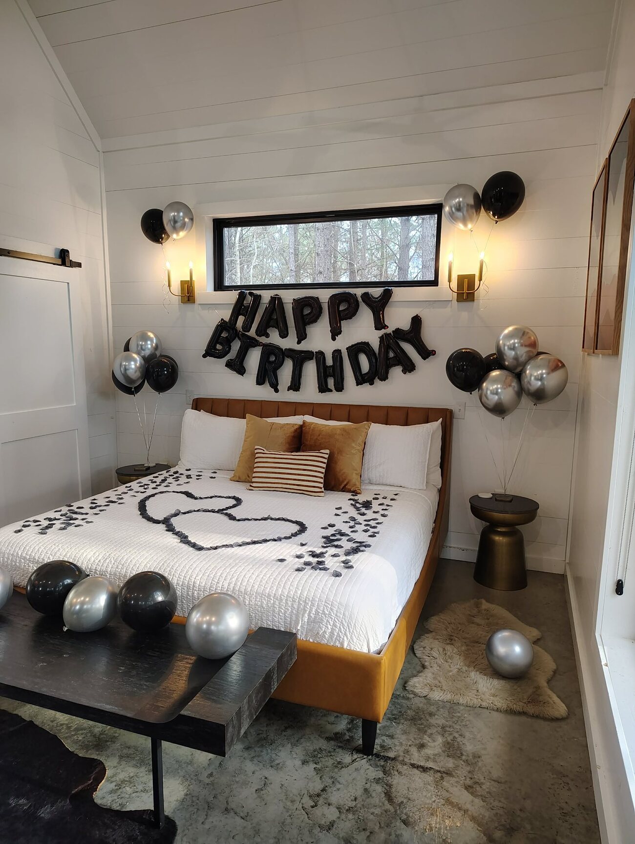Black Happy Birthday balloons and a rose-petal double heart on a bed at The Vine