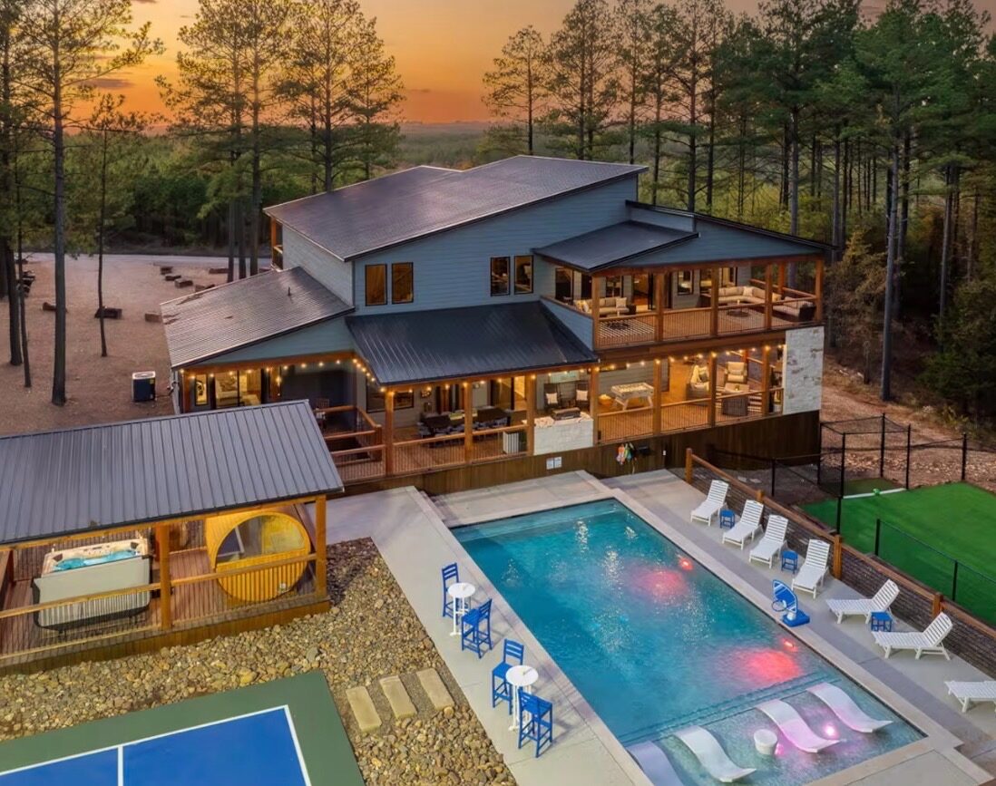 Buy Dirt — an aerial view of a blue-grey cabin with a pool, hot-tub cabana and sport court at sunset