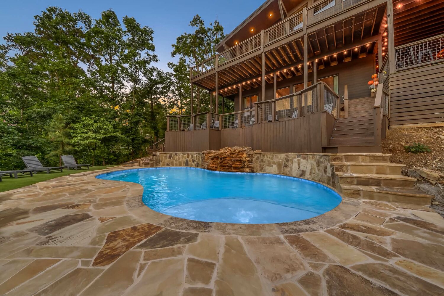 Low-angle view of a flagstone pool deck and blue pool beneath lit cabin balconies