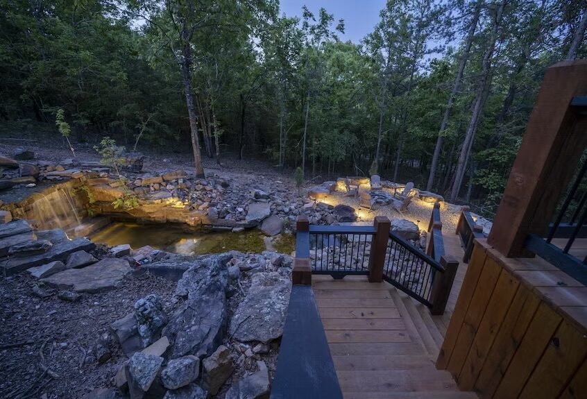 Restoration Falls — a stone waterfall spilling into a pond beside a lit cabin deck