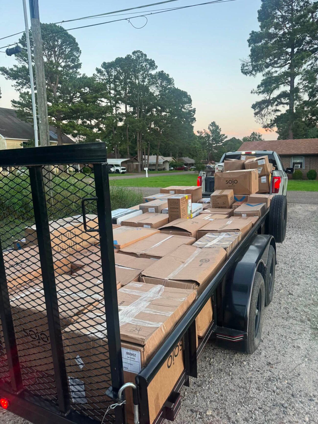 A flatbed trailer and pickup stacked with cabin supply boxes at dusk