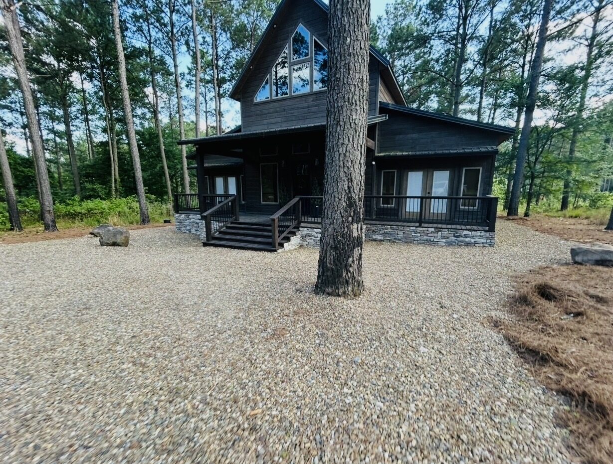 A client cabin set among tall pines with a freshly raked gravel drive and tidy pine straw